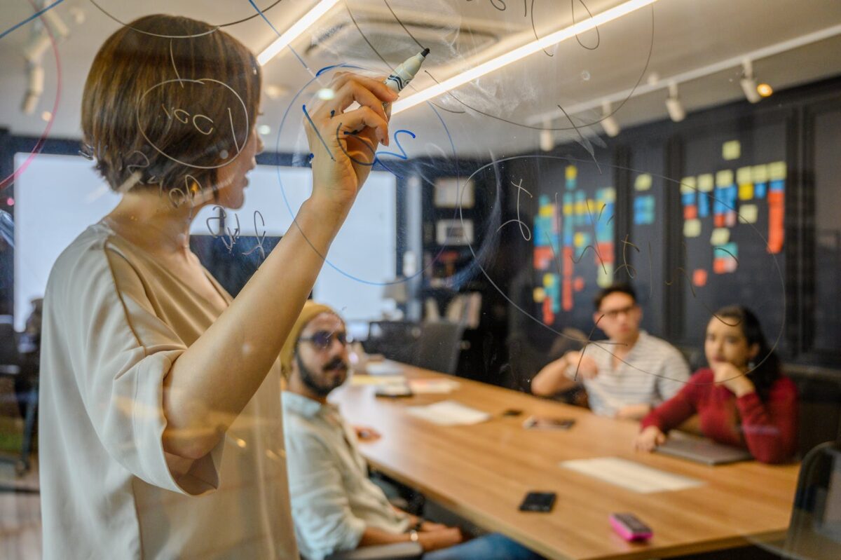 people on a business meeting discussing and writing on clear board