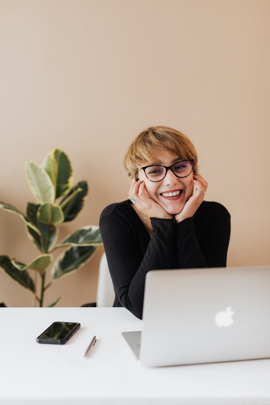 cheerful woman smiling while sitting at table with laptop