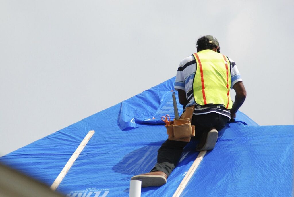 Technician performing an emergency tarp installation on leaking roof.