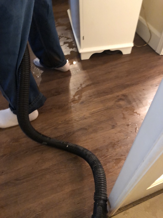 Image of wet Luxury Vinyl Tile while a water damage technician with white socks on only, extracts the water in Vancouver WA.