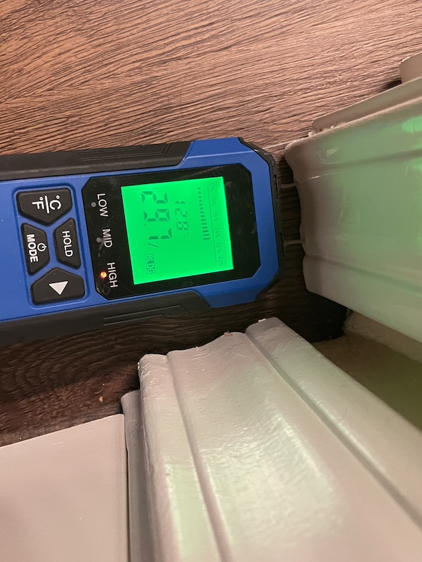 Image of a blue penetrating moisture meter showing a wall is wet, and the display on the meter shows it is 21.3% moisture content