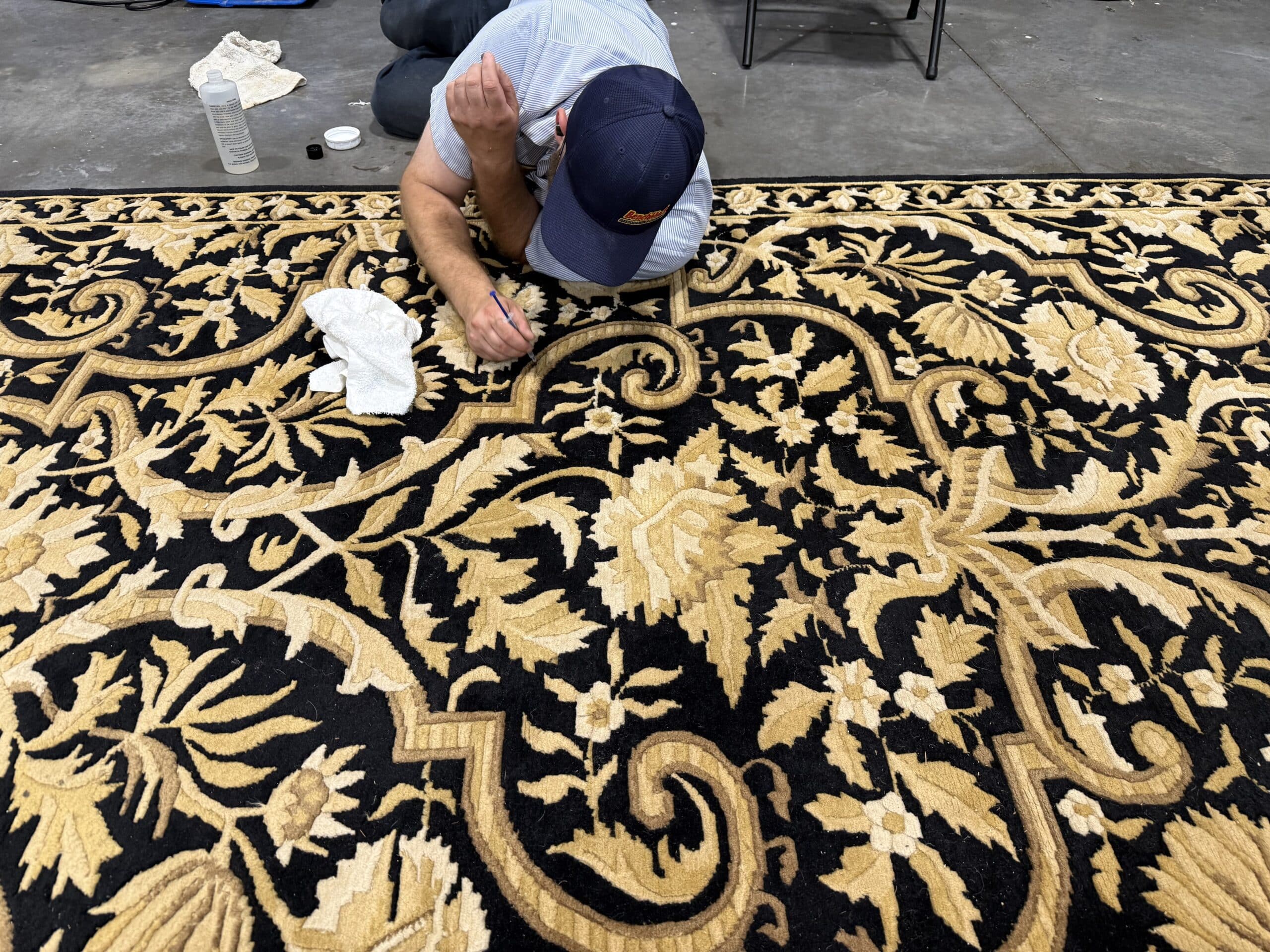 Benchmark Restoration and Cleaning Technician kneeling down and cleaning ink out of a wool area rug